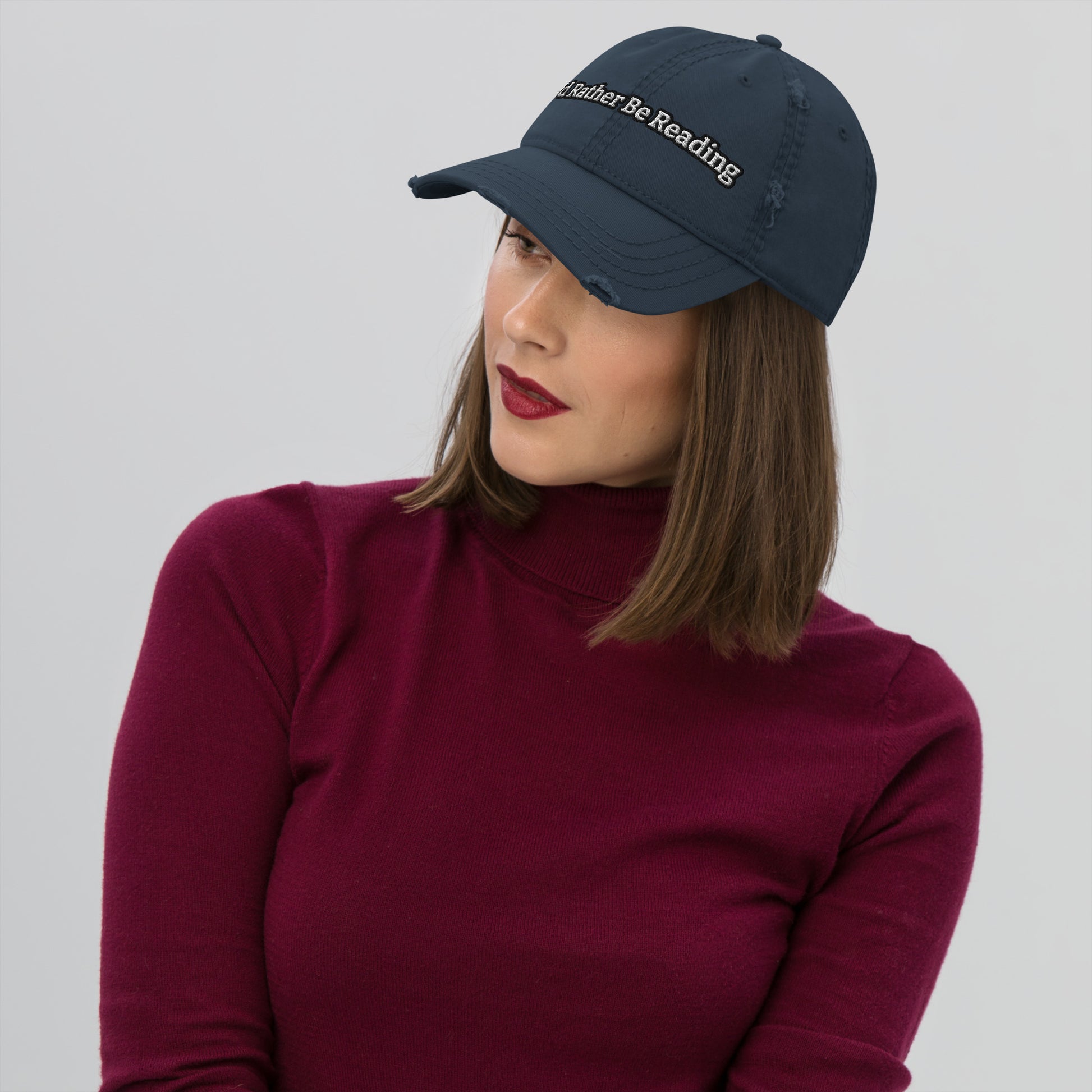 A navy distressed hat with a faded, worn appearance, featuring the text 'I'd rather be reading' in a casual, playful font."